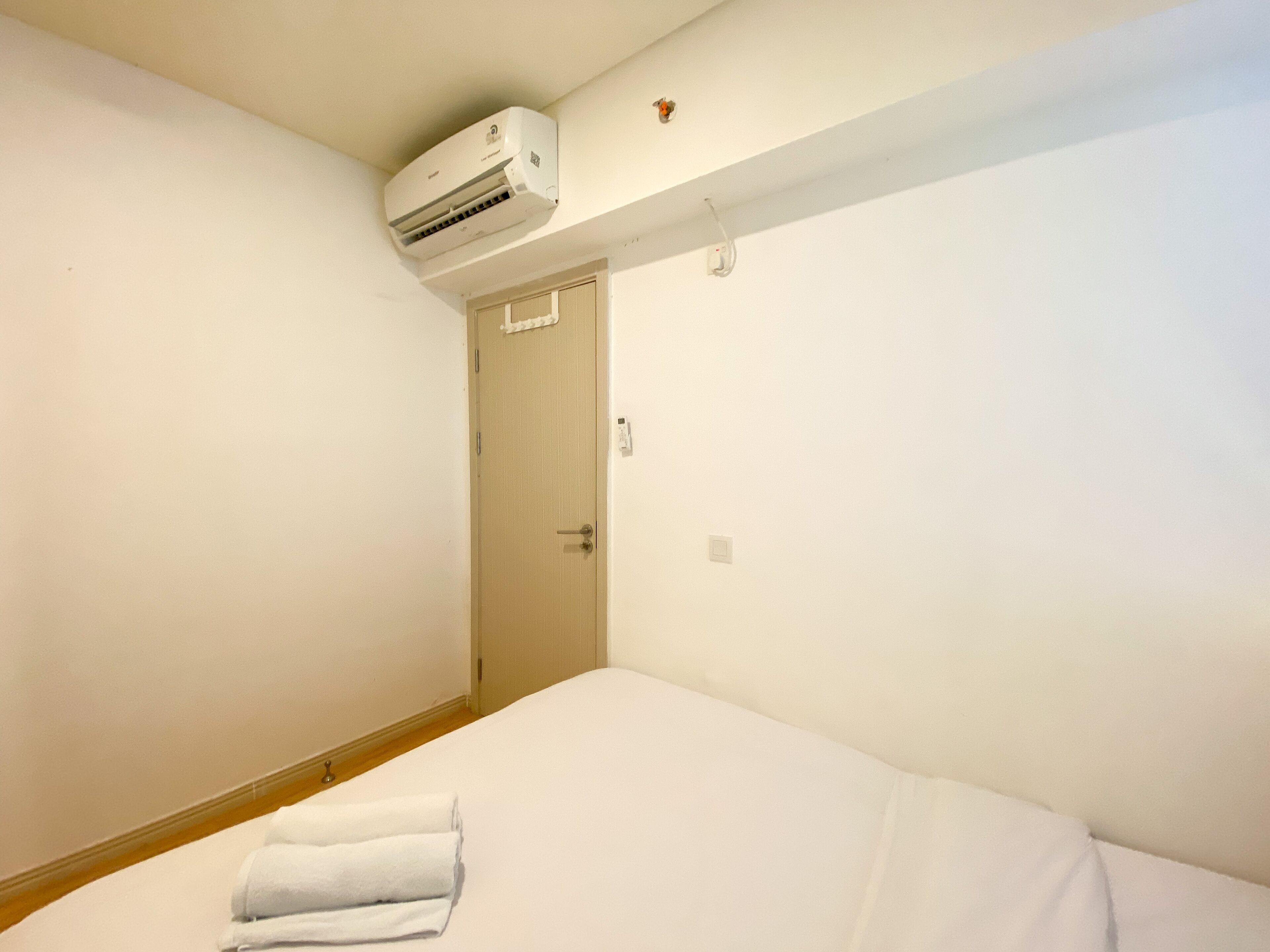 A hotel room with a bed, a door, an air conditioning unit, and a light switch.