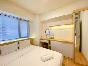 A hotel room with a bed, a desk, a mirror, and a wardrobe. - Nice And Comfy 2Br Apartment At Meikarta (Cikarang)