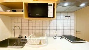 Ett kök med en mikrovågsugn på en hylla, en diskho med ett diskställ och en spis.