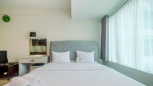 Une chambre d’hôtel avec un lit, deux oreillers, une table de chevet avec une lampe, une horloge au mur et une fenêtre avec des rideaux.