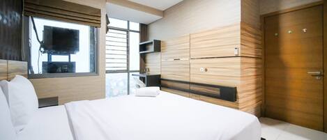 A modern hotel room with a large bed, built-in wardrobe, and a TV mounted on the wall.
