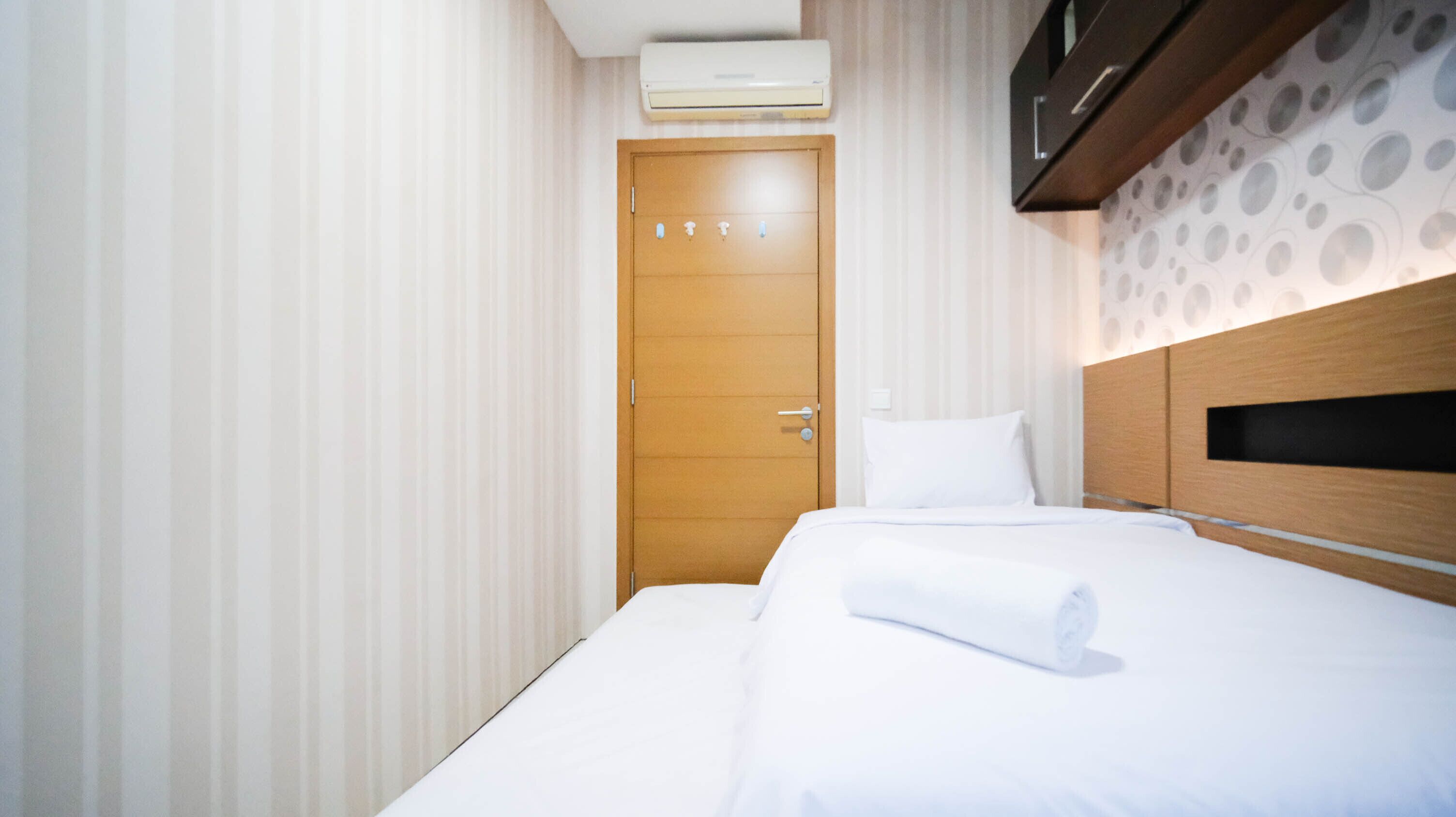Ein Hotelzimmer mit Holztür, einem Bett mit weißen Leinentüchern und einem Kopfteil mit einem Rundmuster.