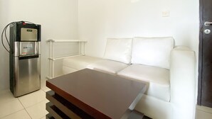 A compact living space with a white sofa, a small wooden table, and a built-in refrigerator. - Simply Look Studio Metropark Condominium Jababeka Apartment (Cikarang)