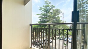 A balcony with a metal railing, a tiled floor, and a view of parked cars and trees. - Simply Look Studio Metropark Condominium Jababeka Apartment (Cikarang)