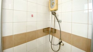 A bathroom with white tiled walls, a shower with a beige control panel, and a brown horizontal stripe. - Simply Look Studio Metropark Condominium Jababeka Apartment (Cikarang)