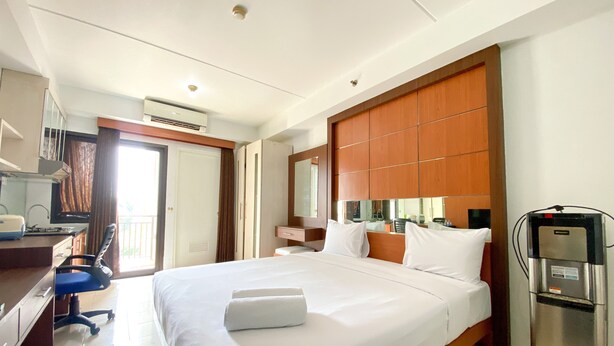 A hotel room with a large bed, a desk with a chair, a minibar, and a bathroom with a shower. - Simply Look Studio Metropark Condominium Jababeka Apartment (Cikarang)