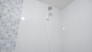 Um chuveiro com um chuveiro manual fixado na parede, área de chuveiro revestida com azulejos e um canto do quarto com outro padrão de azulejos.
