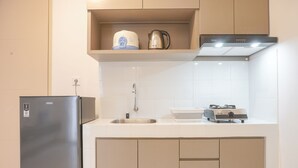 Uma cozinha compacta com geladeira de aço inoxidável, pia, chaleira e cozedor de arroz na bancada.