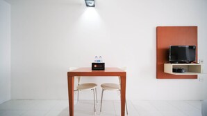 Una habitación pequeña con una mesa de madera, dos sillas, un televisor sobre una estantería y un dispensador de agua en la mesa.
