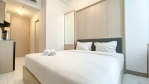 A hotel room with a large bed, two pillows, a headboard, a mirror, and a door.