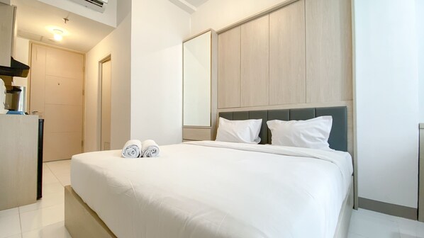 A hotel room with a large bed, two pillows, a headboard, a mirror, and a door.
