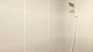 Ein Eckbereich eines Badezimmers mit weißen Fliesen und einer an der Wand befestigten Duschbrause.
