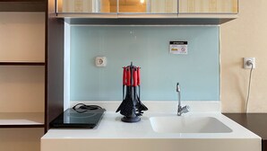 Una cocina con encimera blanca, un lavamanos, un hervidor negro y un hervidor eléctrico rojo y negro.