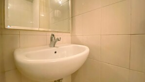 Un baño con lavamanos blanco, espejo y paredes con azulejos.