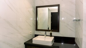 A bathroom with a white marble sink, a dark countertop, and a mirror with a dark frame. - Nice And Fancy 1Br At Branz Bsd City Apartment (Pagedangan)