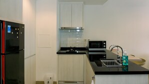 A compact kitchen with a black refrigerator, a microwave, and a stove. - Nice And Fancy 1Br At Branz Bsd City Apartment (Pagedangan)