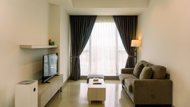 A modern living room with a flat-screen TV, a sofa, a coffee table, and a lamp. - Nice And Fancy 1Br At Branz Bsd City Apartment (Pagedangan)