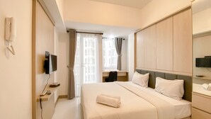 Quarto de hotel com cama, televisão, secretária e cadeira.