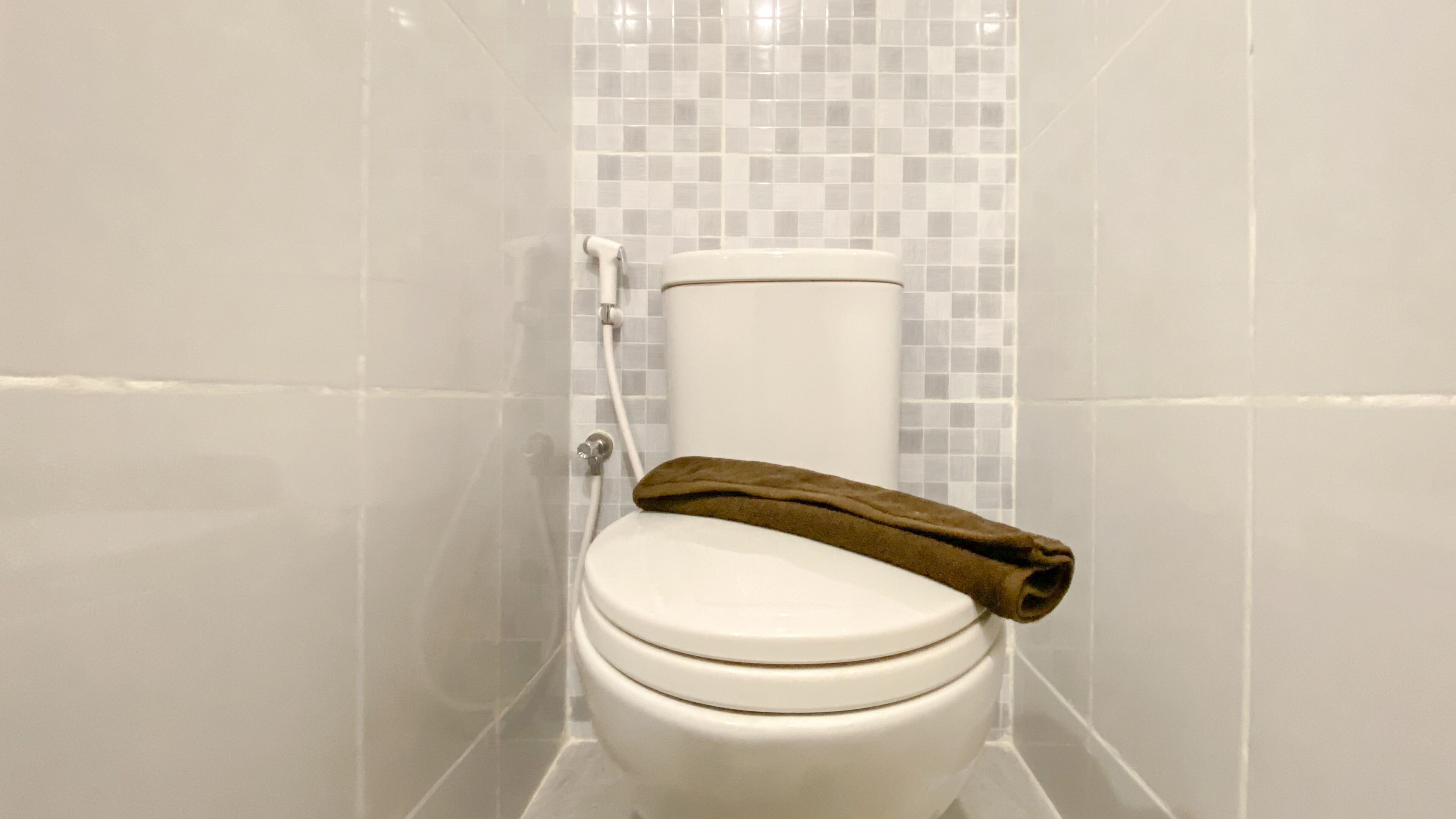 A white toilet with a brown towel on the seat, set against a tiled wall with a checkered pattern.
