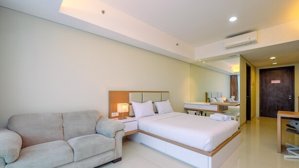 A modern hotel room with a bed, a sofa, a desk, and a mirror.