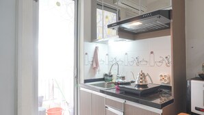 A kitchen with a black countertop, stainless steel sink, and a range hood. There is a window with a view of the outside, and a wooden stool is visible.