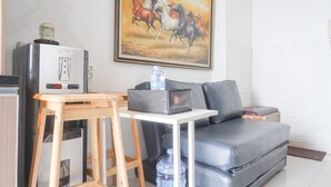 A living area with a sofa, a small table, a water dispenser, and a refrigerator.