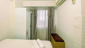 A hotel room with a bed, a wooden nightstand, an air conditioning unit, and a window with curtains.