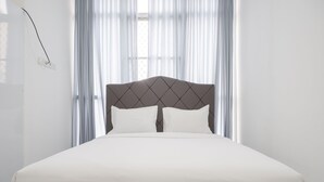 A neatly made bed with a dark headboard and white bedding in a room with sheer curtains and a window. - Exclusive Studio At Gold Coast Apartment (Jakarta)