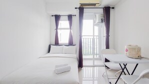 A hotel room with a bed, a table, chairs, an air conditioning unit, and a view through a window with curtains.