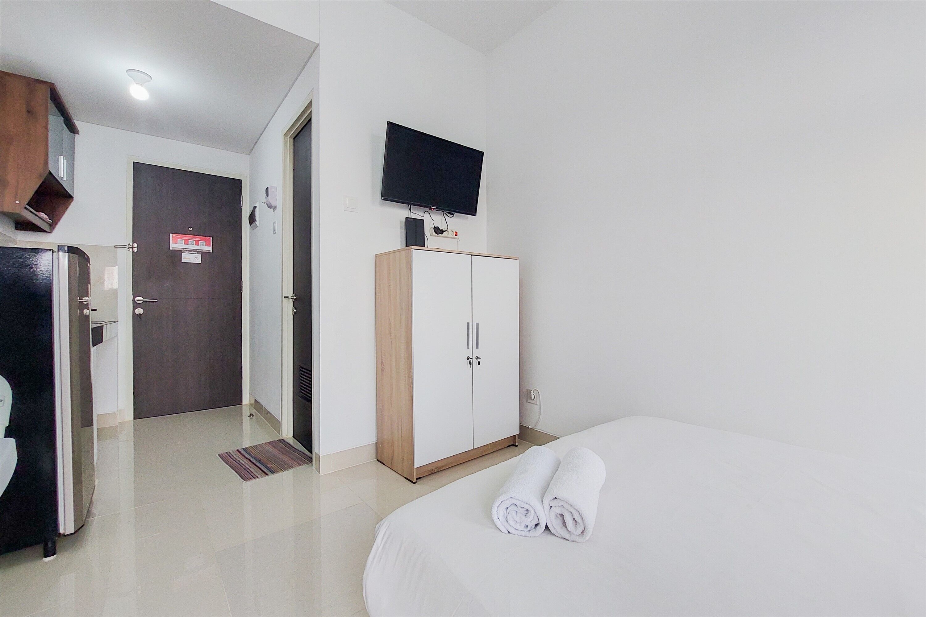 A hotel room with a bed, a wardrobe, a television mounted on the wall, and a door with a sign.