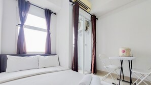 A hotel room with a bed, two rolled towels, a small table with a chair, and a window with curtains.