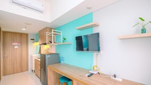 A modern kitchen with a wooden countertop, a built-in fridge, a TV mounted on the wall, and a small plant on a shelf. - Homey And Simply Look Studio Room At Bogor Icon Apartment (Bogor)