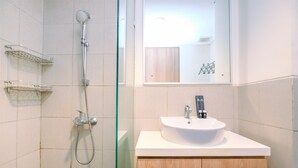 A modern bathroom with a glass shower enclosure, a white sink with a mirror above it, and wooden cabinets. - Homey And Simply Look Studio Room At Bogor Icon Apartment (Bogor)