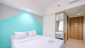 A modern hotel room with a bed, white bedding, a teal accent wall, a wooden door, and a mirror. - Homey And Simply Look Studio Room At Bogor Icon Apartment (Bogor)