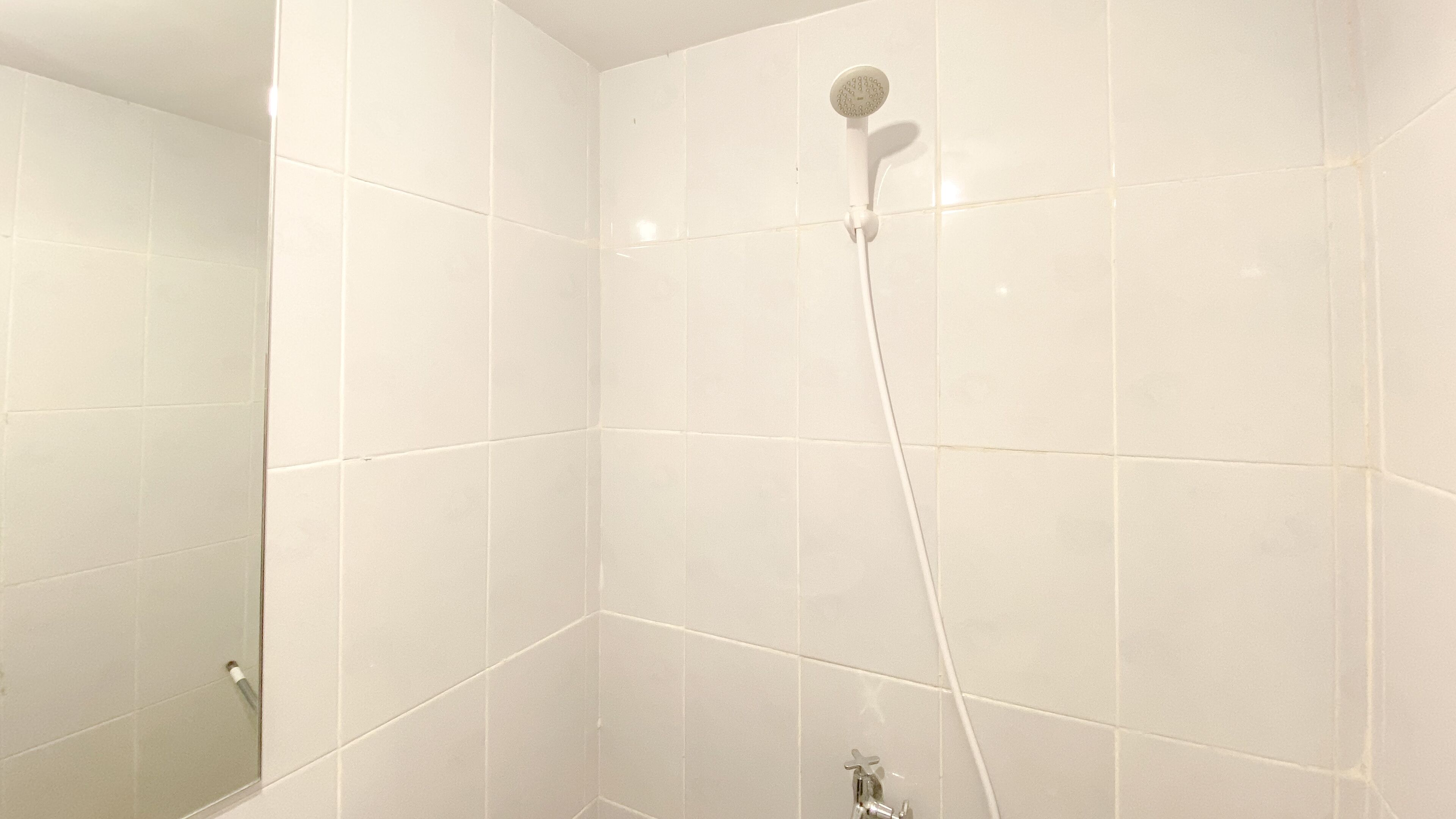 Une salle de bain avec des murs recouverts de carreaux blancs et une douche équipée d’un pommeau de douche amovible.