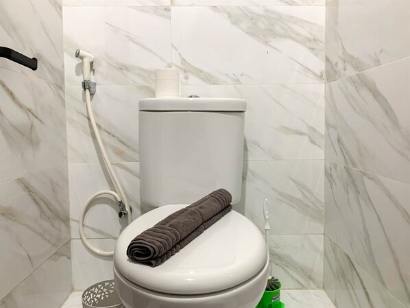 A bathroom with a toilet, a toilet paper holder, a hand dryer, and a green cleaning brush.