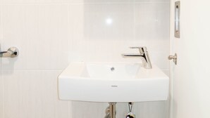 A white bathroom sink with a chrome faucet, a mirror above it, and a wooden cabinet in the background. - Elegant And Cozy Studio Barsa City Apartment (Depok)