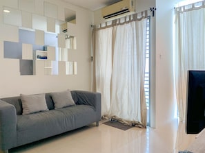 A modern living room with a grey sofa, a flat-screen TV, and a large window with curtains.