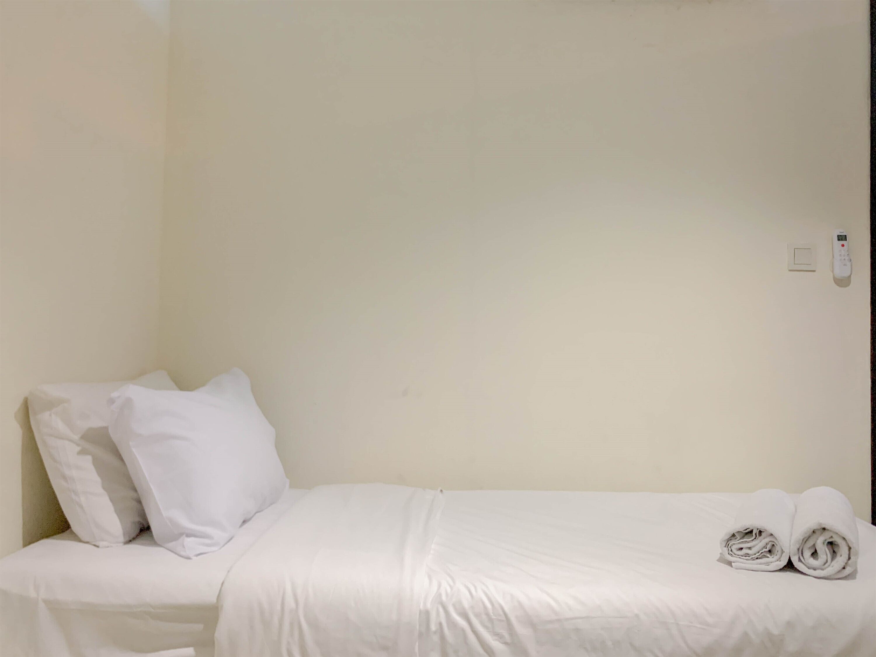 A single bed with white bedding and pillows, a wall-mounted light switch, and a telephone.