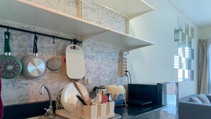 Een moderne keuken met een marmeren achterwand, een roestvrijstalen spoelbak en een inbouwoven. Er staat een zwarte televisie op een dressoir en een grijze bank in de woonkamer.