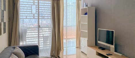 Una sala moderna con un sofá gris, un televisor sobre un mueble de madera y un ventanal con cortinas.
