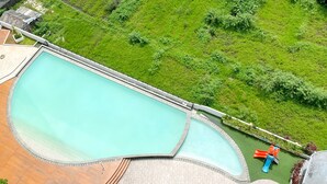 A large swimming pool with a slide, surrounded by a paved deck and lush greenery. - Great Choice And Comfort Stay 2Br At Patraland Urbano Apartment (Bekasi)