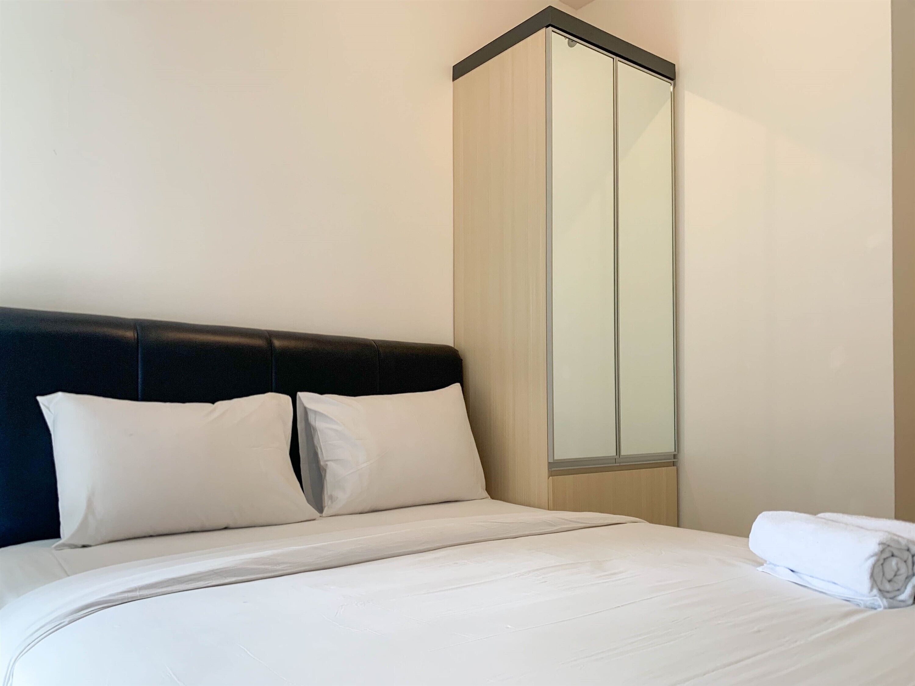 Una habitación de hotel con una cama, cabecero negro y un armario espejo grande.