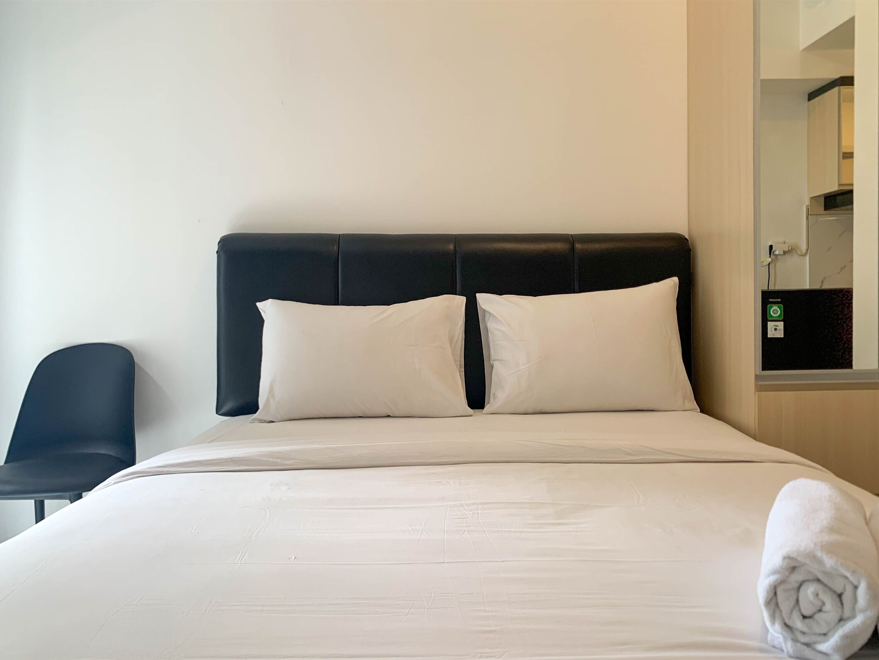 A hotel room with a bed, two pillows, a black chair, and a bathroom mirror.