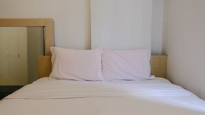 A neatly made bed with white bedding and two pillows, a wooden headboard, and a mirror on the wall. - Good Choice 2Br At 12Th Floor Gateway Ahmad Yani Cicadas Apartment (Bandung)