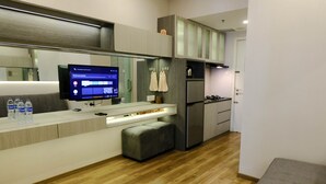A modern kitchen with a built-in TV, wooden flooring, and grey cabinetry. - Homey 1Br At Apartment Parahyangan Residence (Bandung)