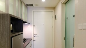 A compact kitchen with a built-in stove, a microwave, and a refrigerator. There is a white door with a small window and a light switch on the wall. - Homey 1Br At Apartment Parahyangan Residence (Bandung)