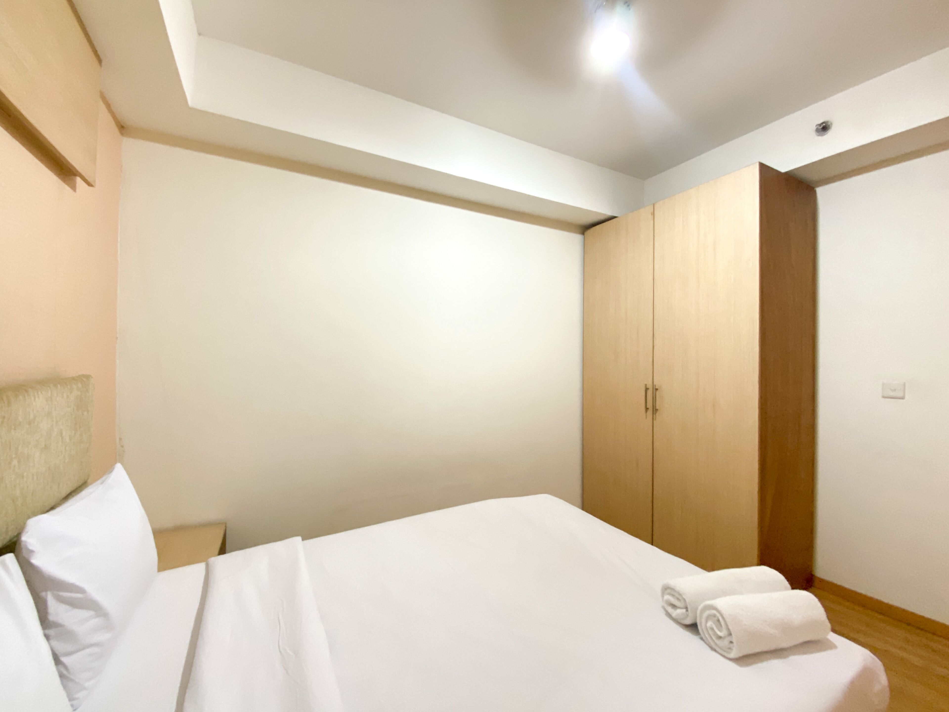 A hotel room with a bed, a wooden wardrobe, and a ceiling light.