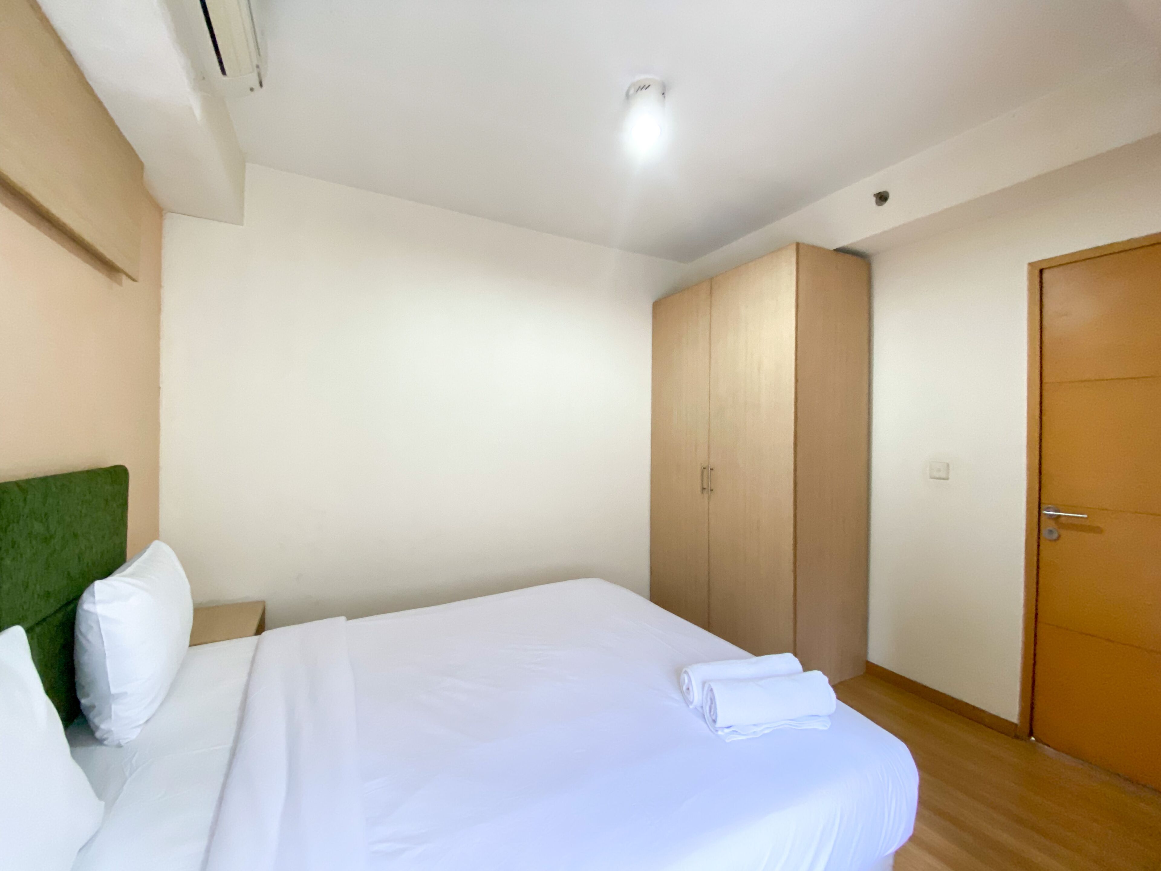 Quarto de hotel com uma cama, cabeceira verde, guarda-roupa e uma porta.