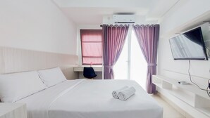 Habitación de hotel con cama, escritorio, silla, televisor y aire acondicionado.